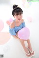 A young girl sitting on the floor holding a pink balloon.