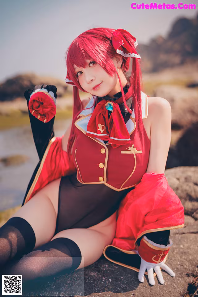A woman in a red and black outfit sitting on a rock.