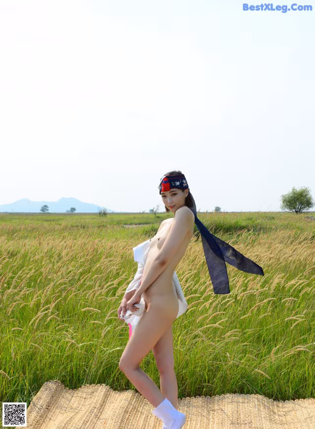 A naked woman standing in a field of tall grass.