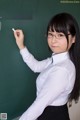 A woman in a school uniform writing on a blackboard.