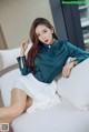 A woman sitting on a white couch wearing a green blouse.