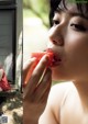 A woman eating a slice of watermelon in front of a window.