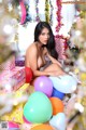 A naked woman sitting on top of a pile of balloons.