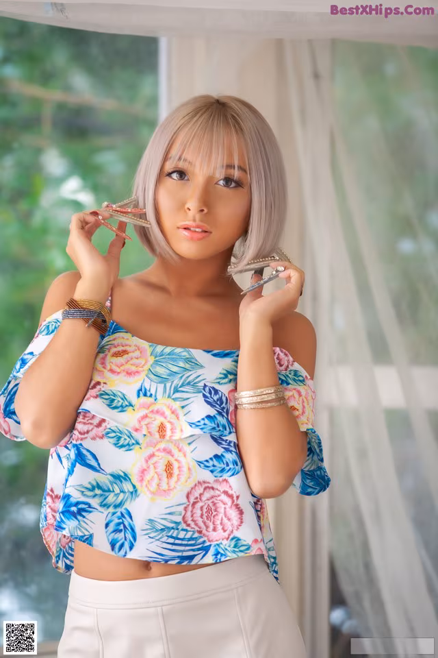A woman in a floral top and white skirt posing for a picture.