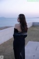 A woman in a black dress standing by the ocean.